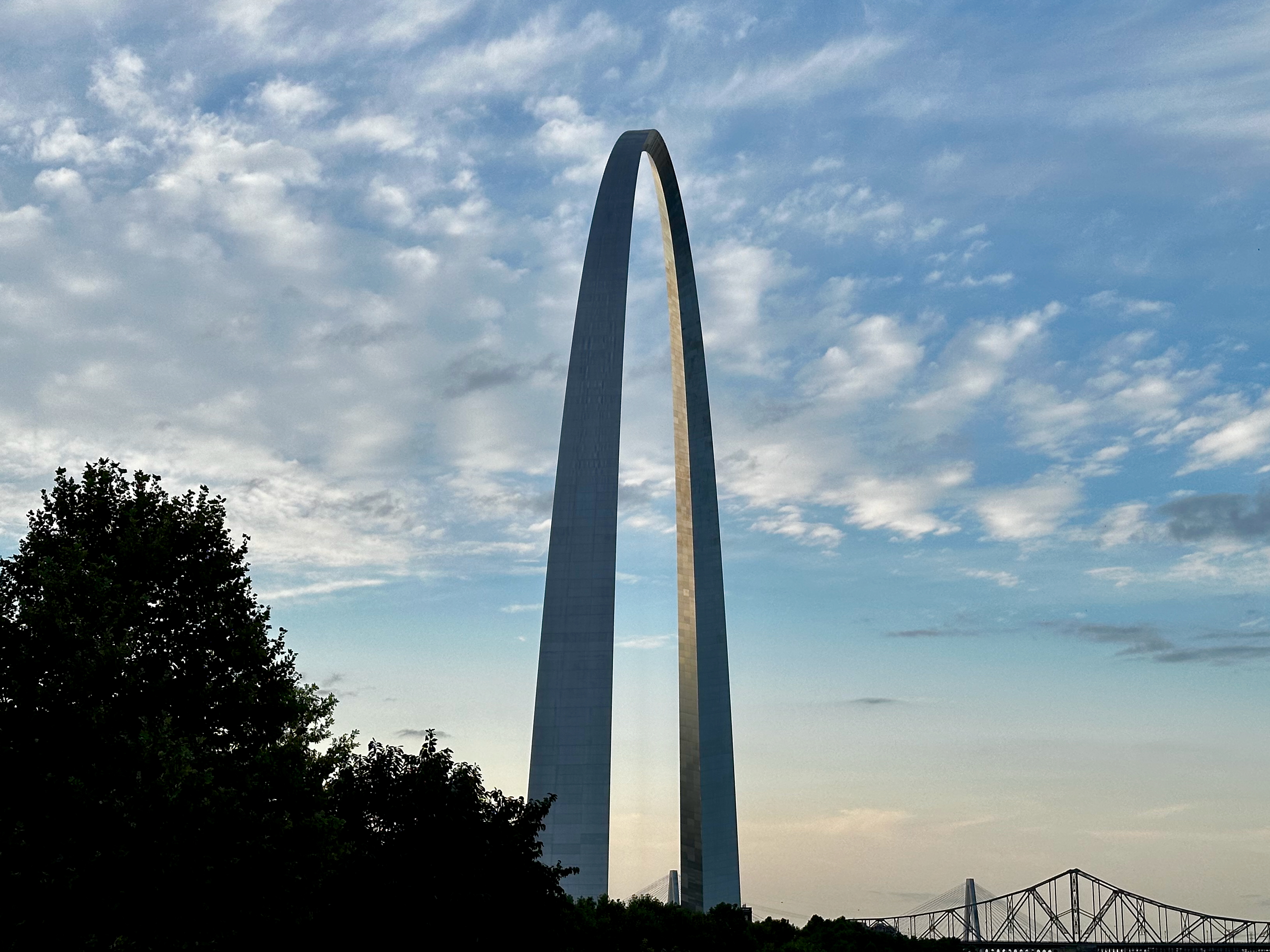 The St Louis Arch as seen from the side near sunset with some trees in the foreground