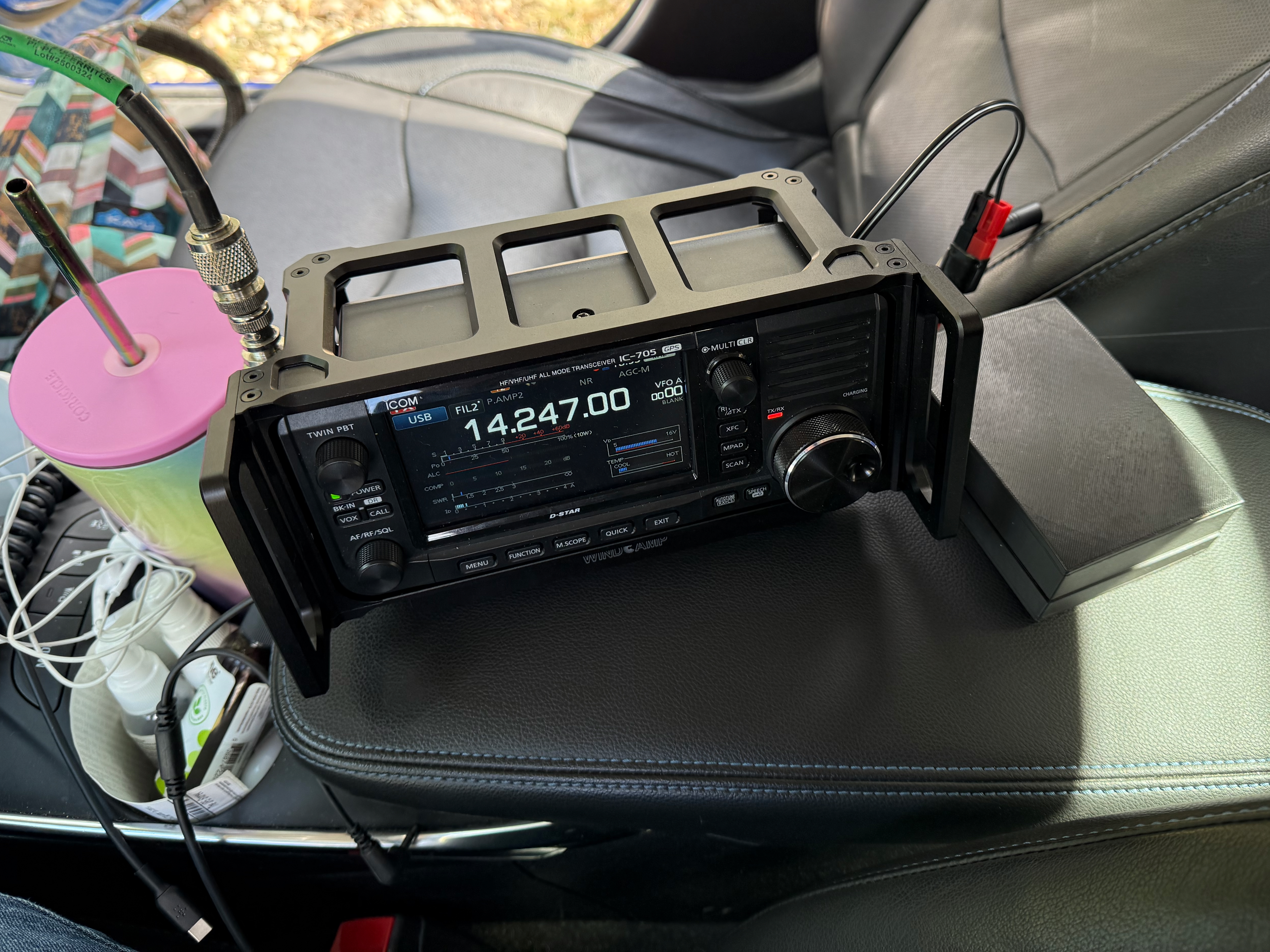 The setup in the car. An Icom IC-705 on the center armrest of the car with the antenna coax off to the right and an empty carseat with an open door in the background.