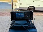 A view from the first activation attempt. An Icom IC-705 on a kneeboard in the foreground, a concrete sidewalk in the background with a brick sidewalk and street beyond that