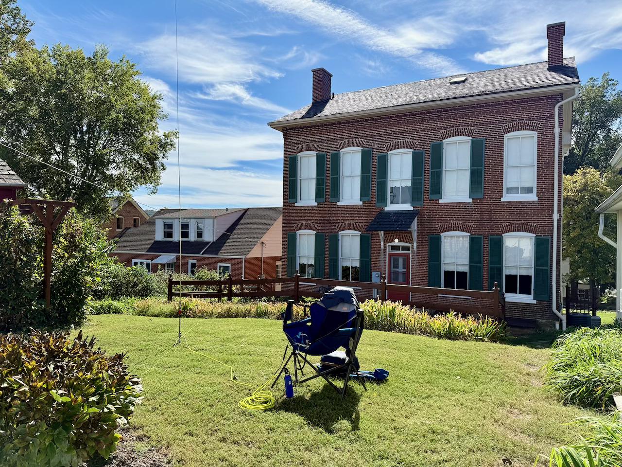 A view from the second try. A small patch of grass with a camping chair and vertical antenna in the foreground and an old two story historic brick building in the background