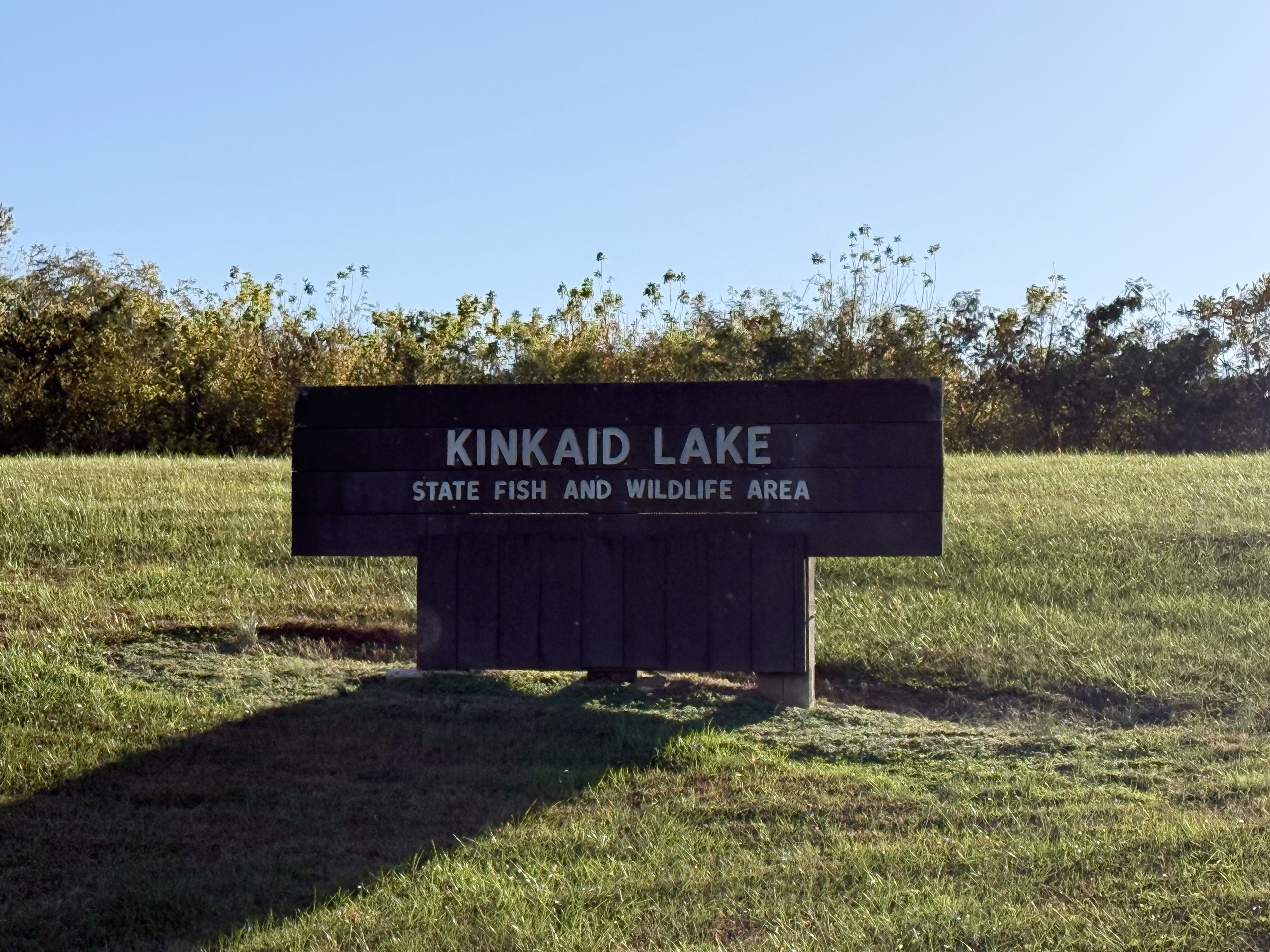 A large wood park sign on a grassy hill the reads KINKAID LAKE STATE FISH AND WILDLIFE AREA