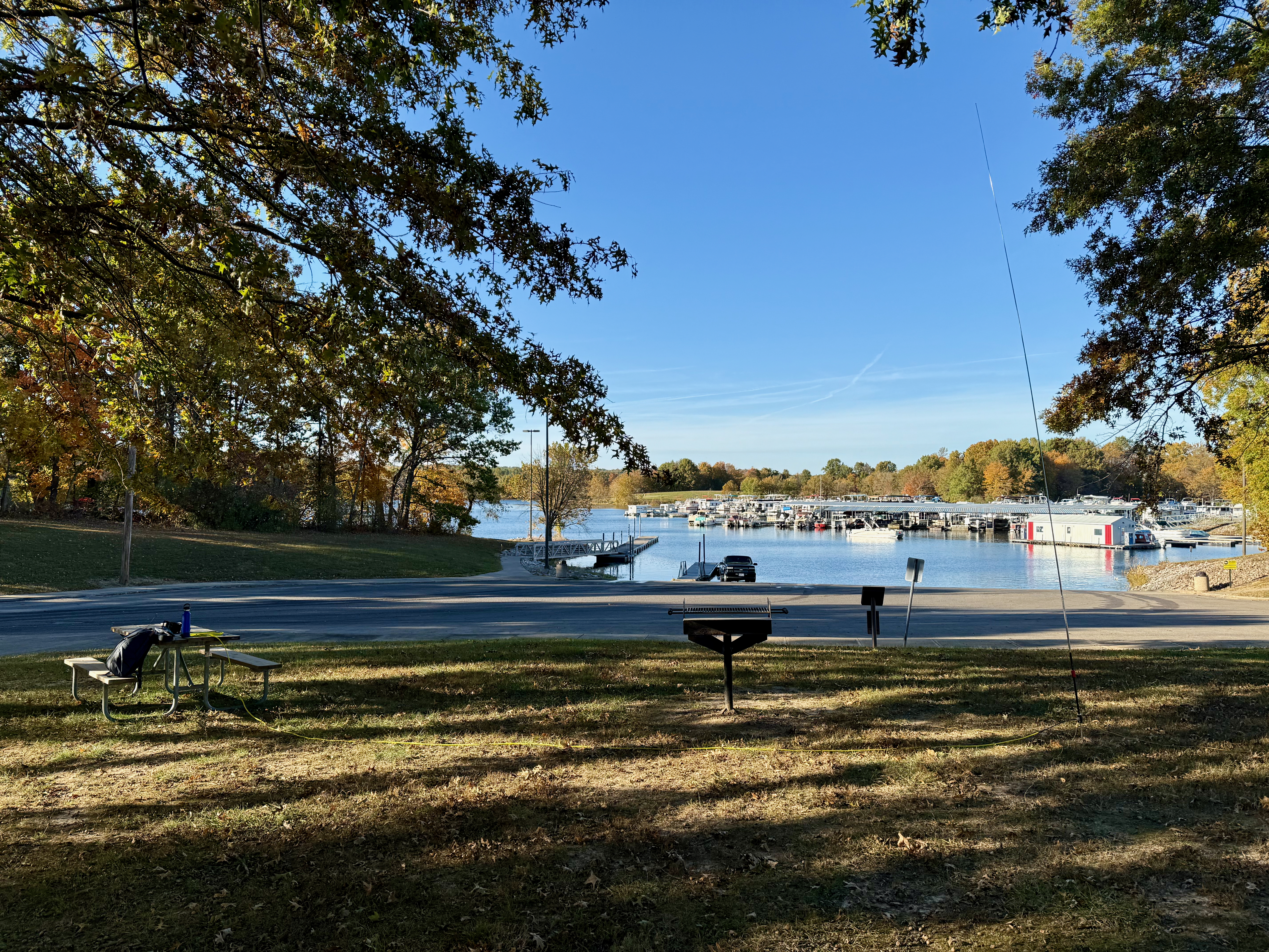 The shady spot in front of the boat ramp I activated from. A park bench on the left, veritcal antenna on the right and the boat ramp with docks in the background under a clear blue sky.