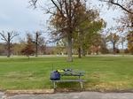 My equipment setup at a picnic table in the park just in front of a parking lot. A large field in the background with some large trees, many of which still have some colorful leaves.