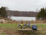 The view from the station setup on a gray, dreary, fall day. In the background is the lake and parking lot for the boat launch. In the foreground is a picnic table with my station and the vertical whip behind that.