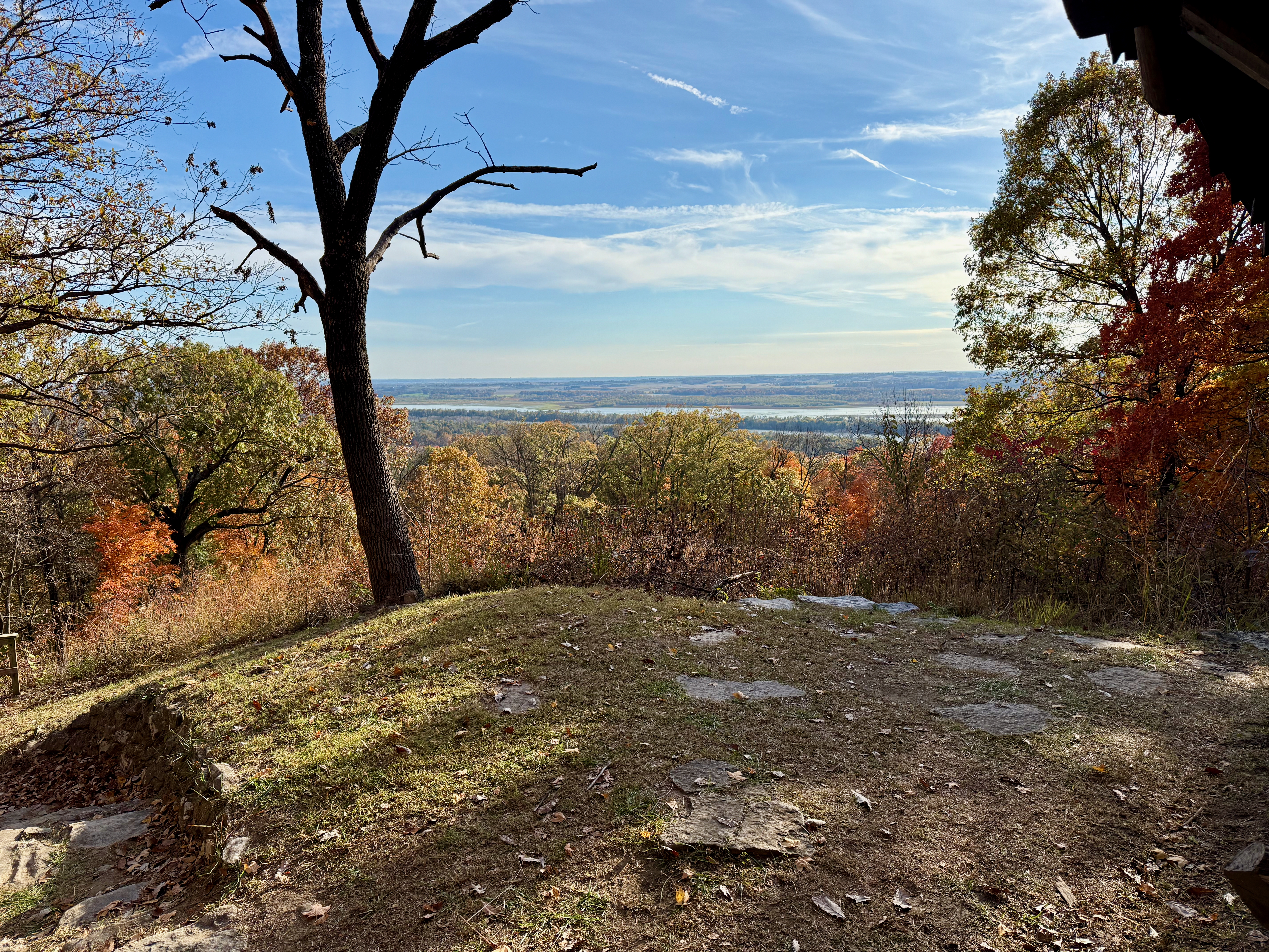 A view from Twin Shelter showing a small patch of rock and grass and a view towards the South over the horizon. The fall trees are various colors of red, yellow, orange and green.