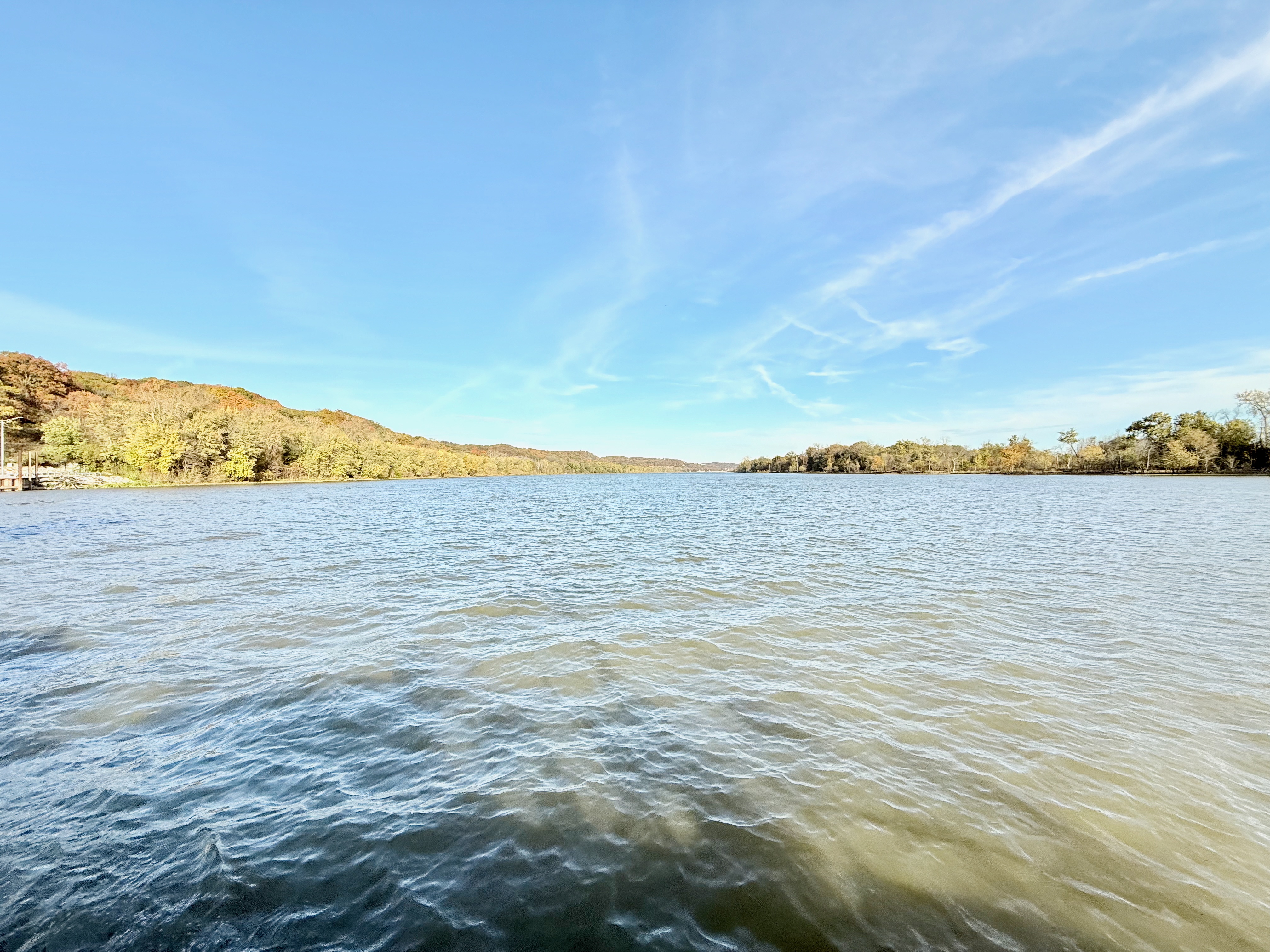 The Illinois river from the ferry. Slightly choppy, grey water leads off into the distance, tree-lined shores on the left and right.